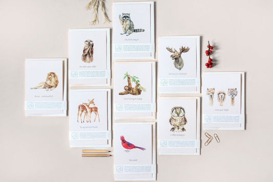 Sample of nine greeting cards with animal illustrations and cute captions laid flat on a plain surface