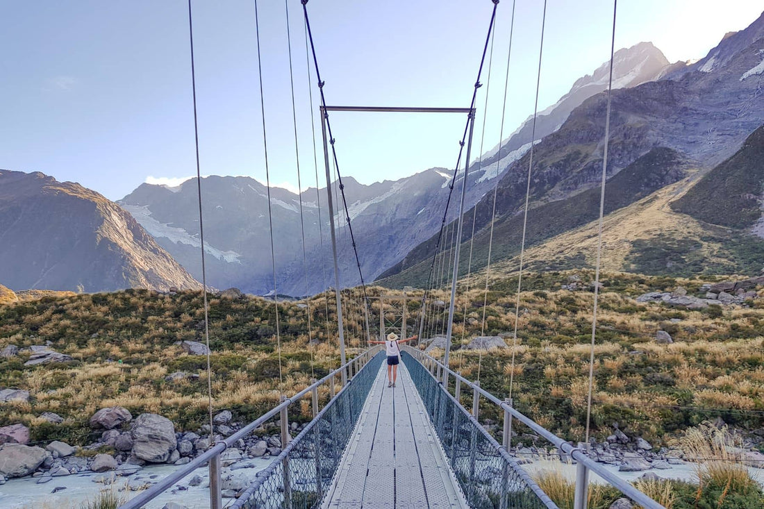Trouvaille founder standing on a bridge admiring a beautiful landscape on the Hooker Valley Track in New Zealand