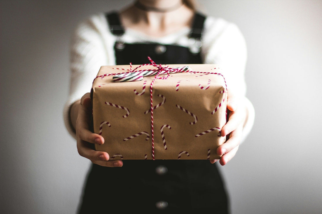 Woman holding a Christmas gift wrapped in brown paper with red string against a neutral background