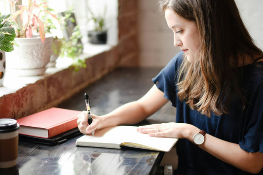 Woman writing in a notebook at a desk by a window, mindful journaling for memory and creativity