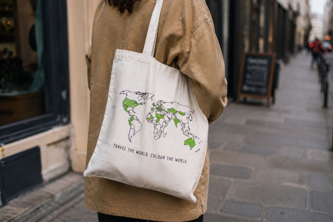 Woman carrying world map colour-in tote bag on a European city street, everyday travel tracker