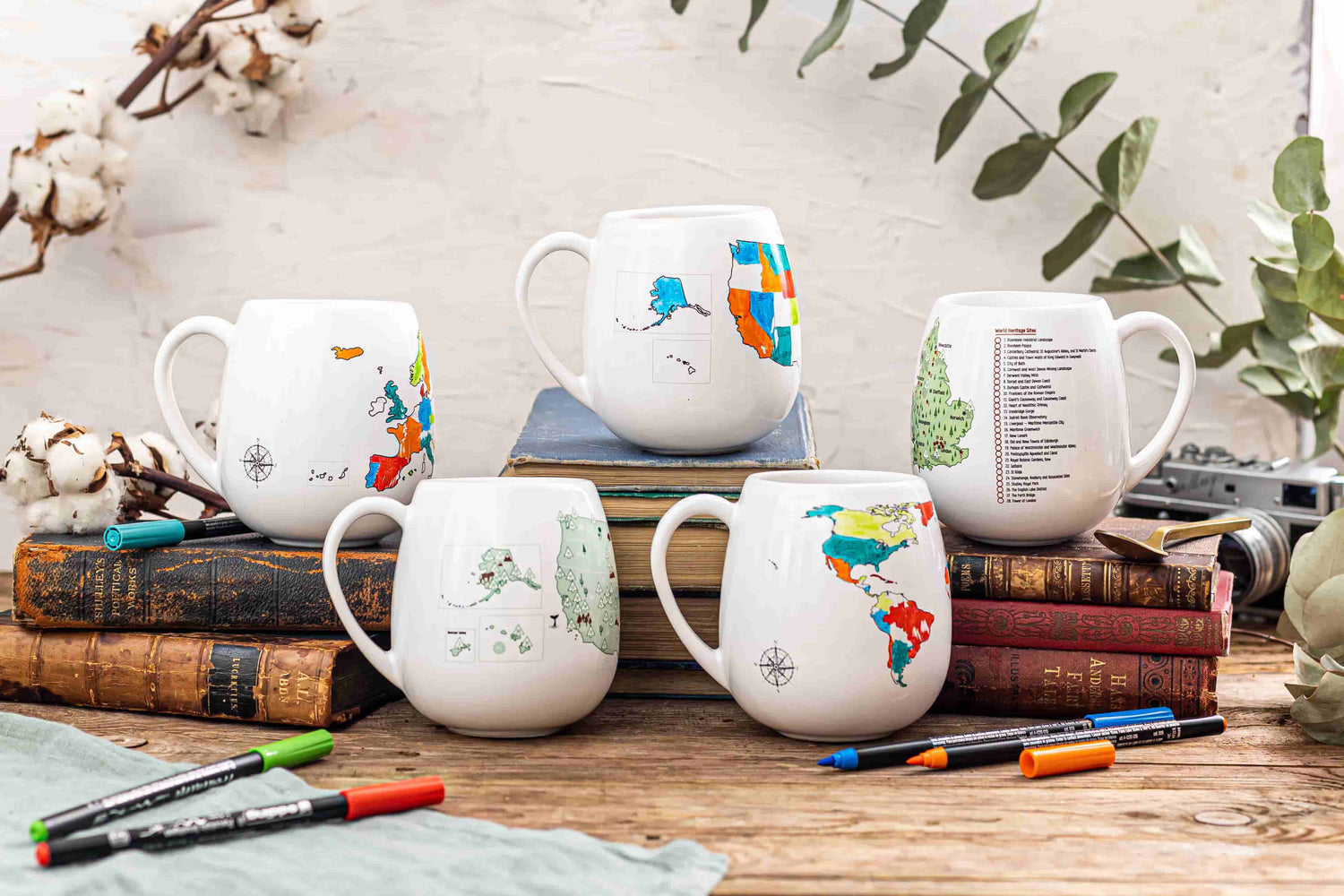 Colour-in mugs collection with colourful ceramic pens on wooden table, travel tracker mugs for adventurers
