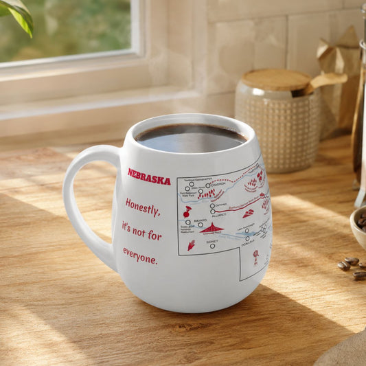 White mug with a Nebraska map design to track trips and experiences placed on a wooden kitchen counter with coffee.