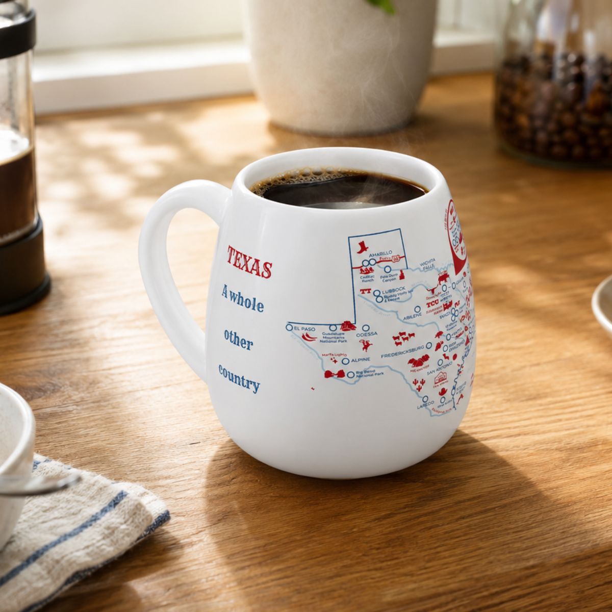 White mug with a Texas map design to track trips and experiences placed on a wooden kitchen counter with coffee.