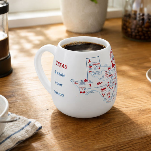 White mug with a Texas map design to track trips and experiences placed on a wooden kitchen counter with coffee.