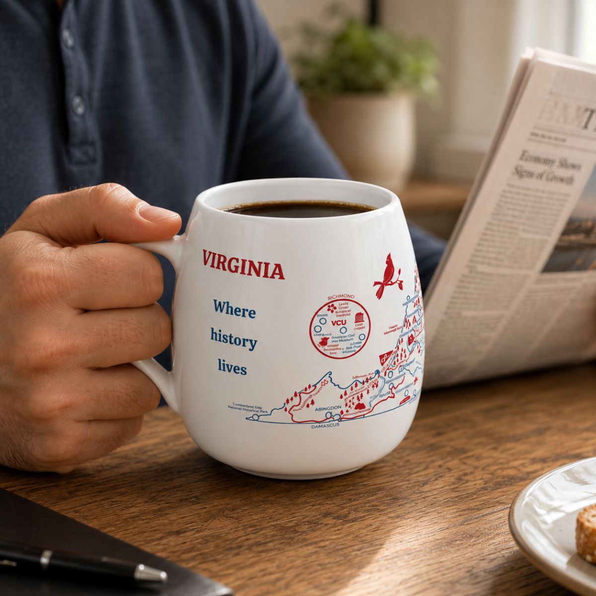 Person holding a Virginia color-in mug filled with coffee, sitting at a table with a newspaper