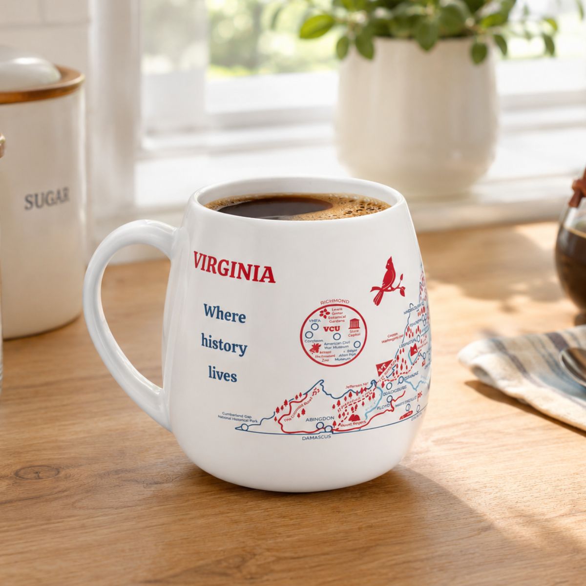 White mug with a Virginia map design to track trips and experiences placed on a wooden kitchen counter with coffee.