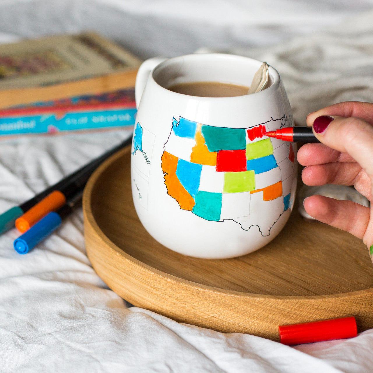 Coloring in visited states with a red ceramic pen on a colored USA mug in a home setting