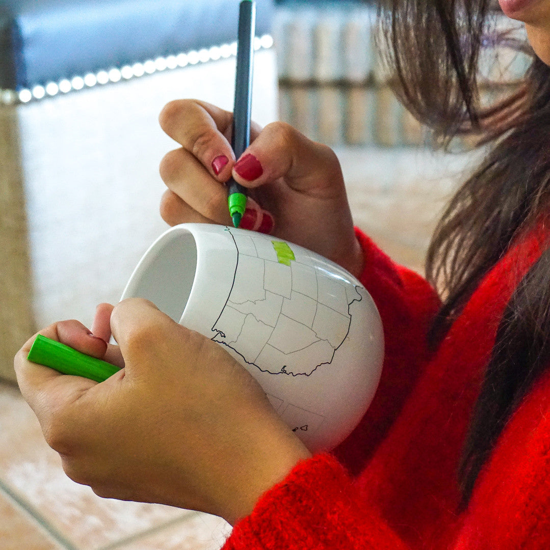 Woman coloring in states on a USA map mug with a green marker to mark states visited, interactive travel tracker mug