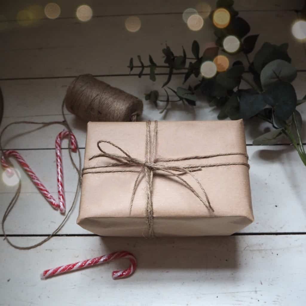 A gift wrapped in eco-friendly kraft paper with a hand-tied bow using natural twine string, set against a wooden background