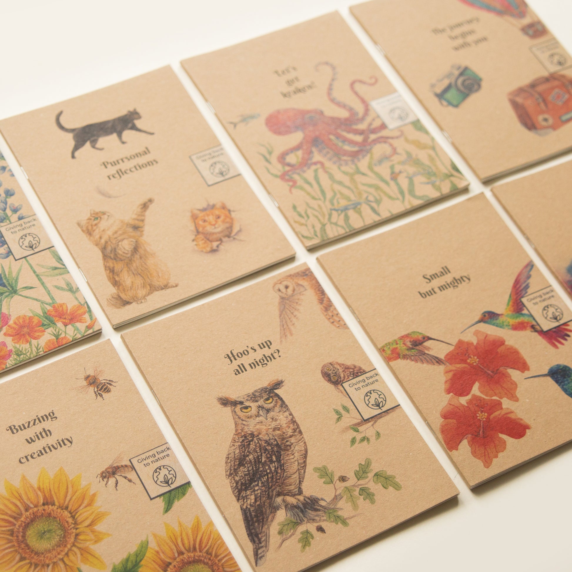 A collection of eco-friendly notebooks with illustrated covers that give back to charity featuring a variety of animals, plants, and other designs