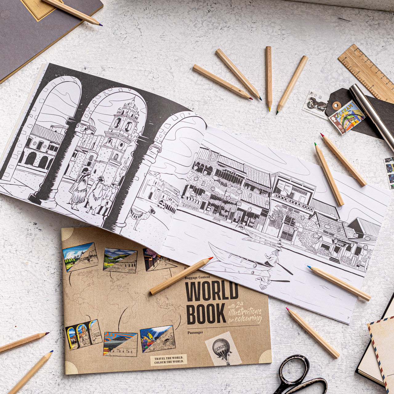 100% recycled world travel colouring book opened with travel illustrations and pencils, sustainable colouring book for travel lovers.