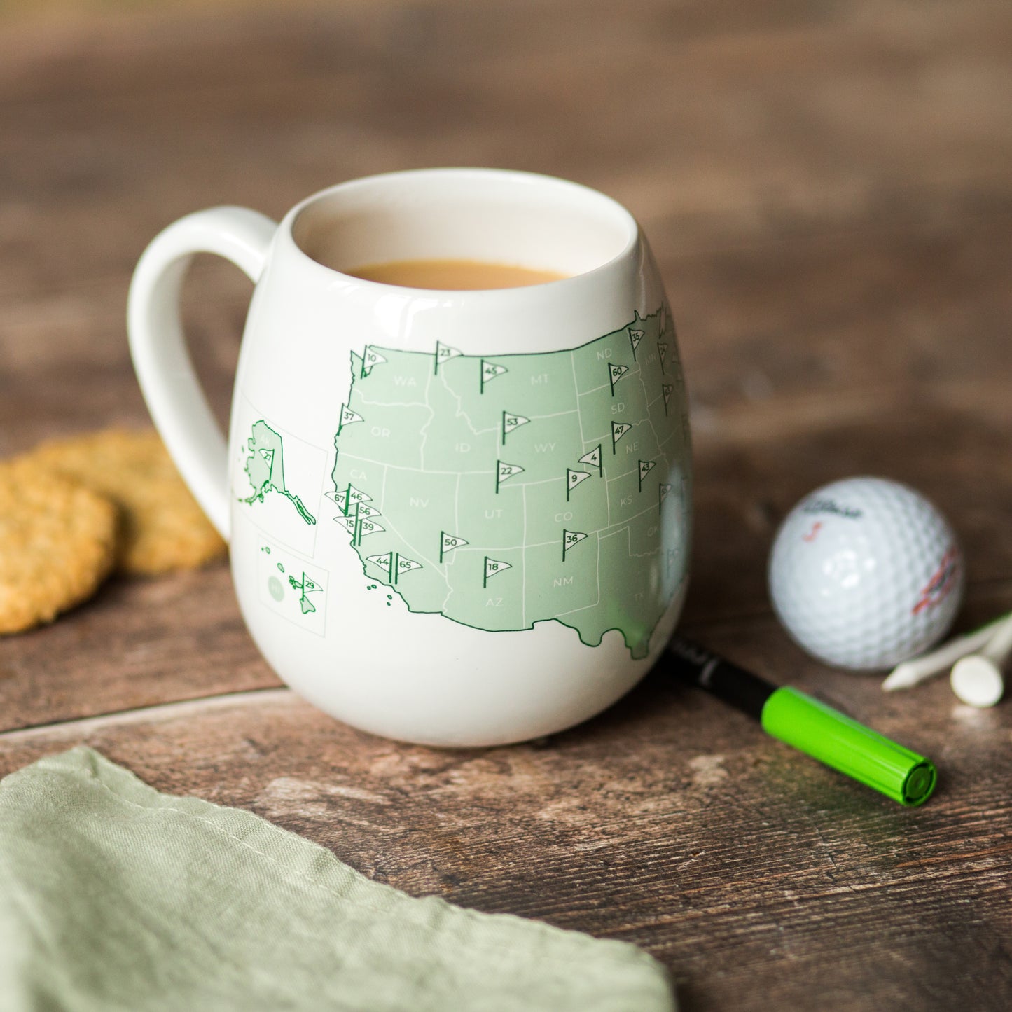 US golfer’s color-in mug showing left side of USA golf courses map beside biscuits and golf ball on a wooden surface, gift for someone who loves golf