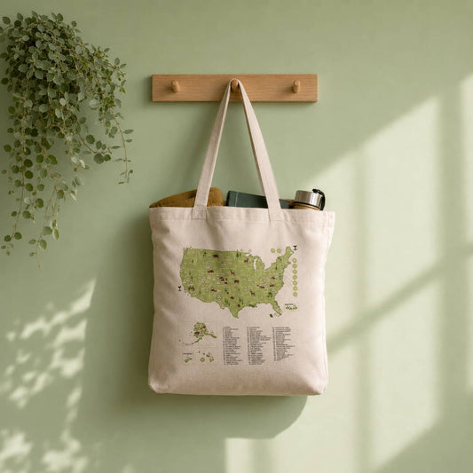 US National Parks tracker tote bag with a USA map design hanging on a wooden hook against a light green wall.