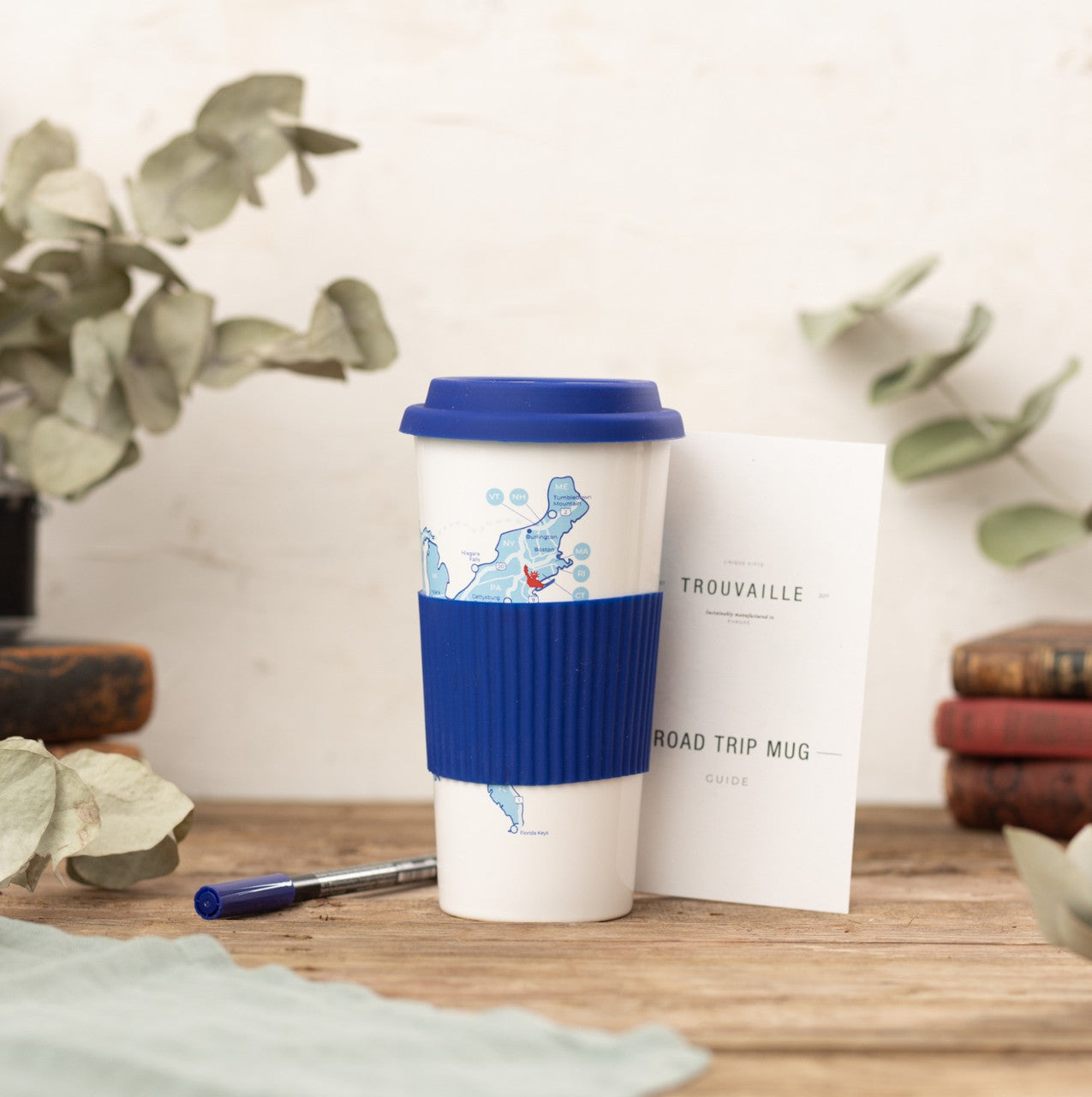 USA road trip travel cup with blue sleeve and lid beside route guide to plan and track completed drives
