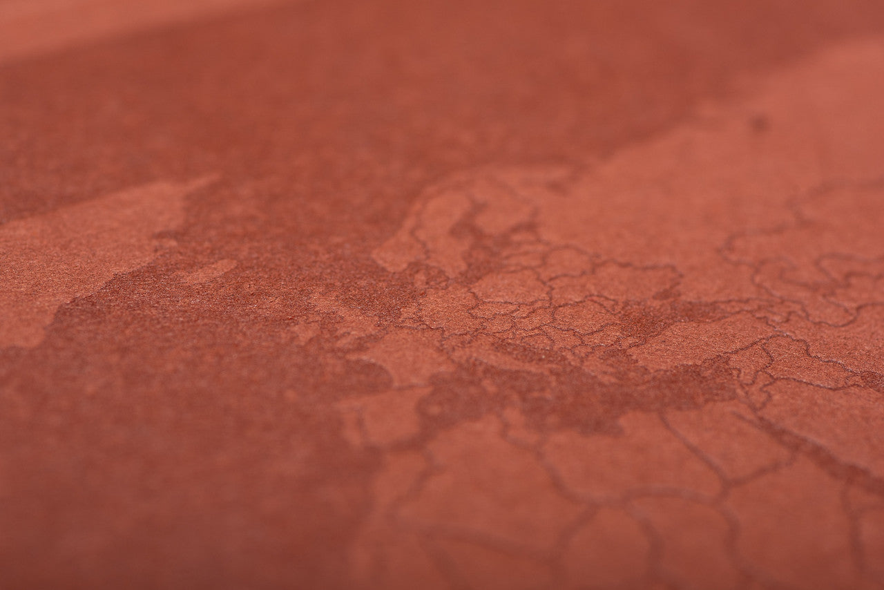 Close-up of letterpressed world map cover on recycled paper travel journal, eco-friendly stationery for travel lovers.